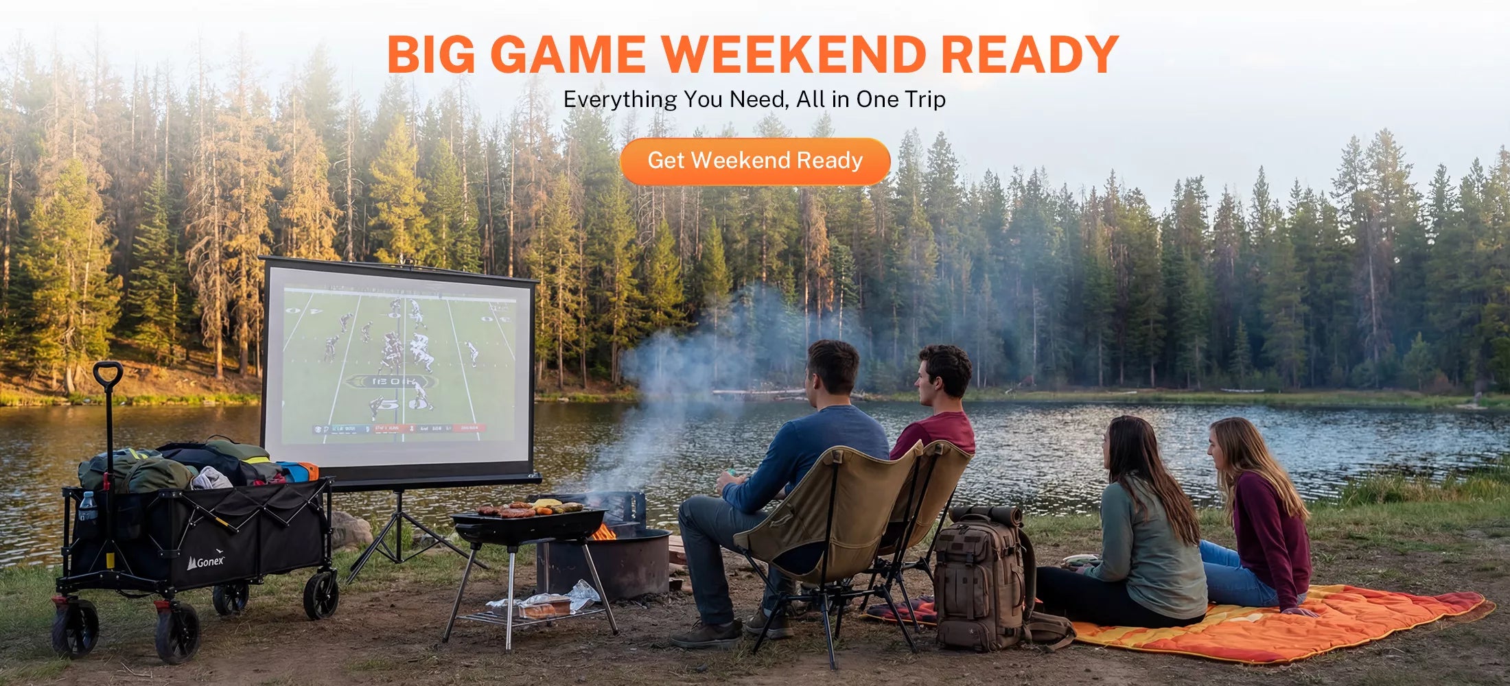Group of people camping by a lake with a projector screen, grill, and cooler.